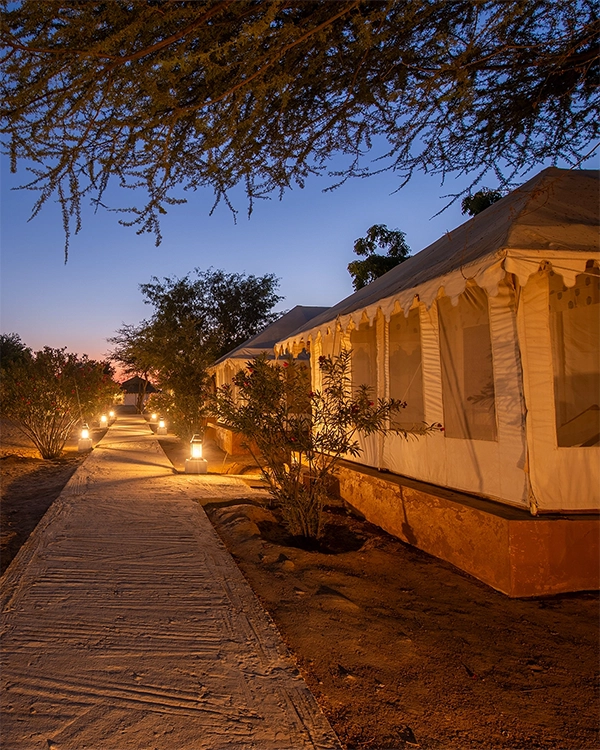 Lantern-lit pathway between luxury tents at Winds Desert Camp at dusk
